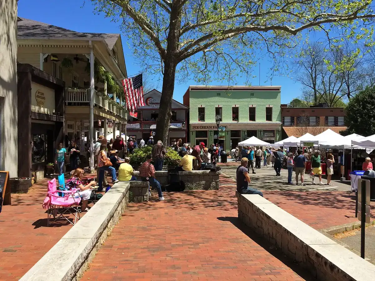 Brick plaza on the Dahlonega public square with people seated along stone walls, white vendor tents and historic storefronts under spring trees